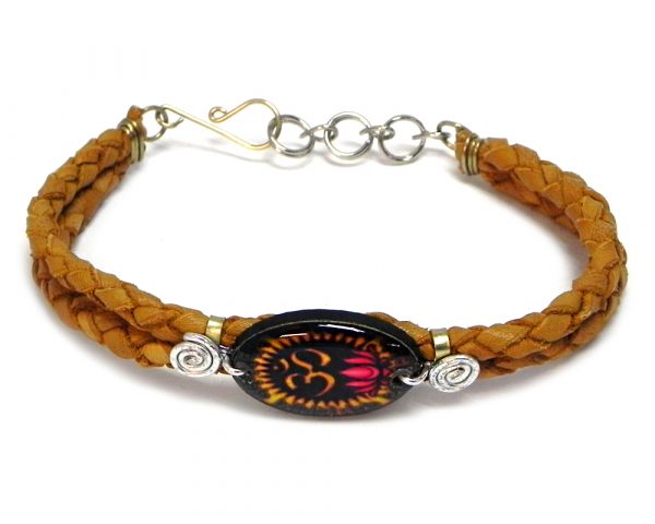 Handmade braided dyed leather bracelet with silver metal wire and oval-shaped acrylic New Age themed om sign lotus flower graphic design centerpiece in tan, brown, gold, black, and hot pink color combination.
