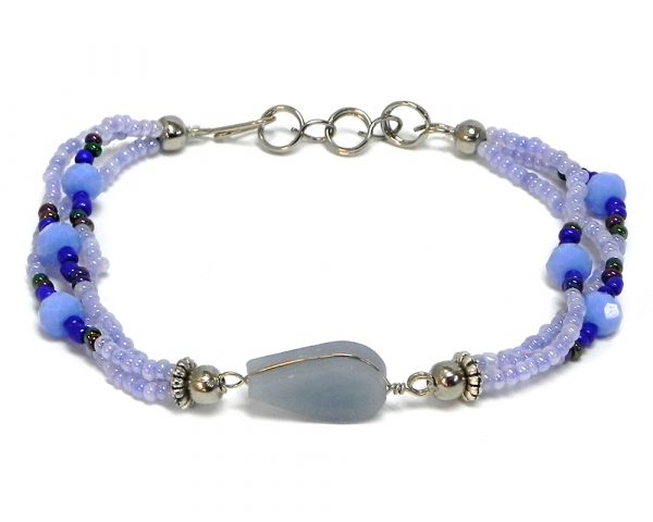 Handmade seed bead and crystal bead multi strand bracelet with teardrop-cut angelite gemstone crystal cabochon centerpiece in light blue periwinkle, blue, and iridescent black color combination.