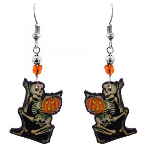 Handmade Halloween themed skeleton holding pumpkin graphic acrylic dangle earrings with beaded metal hooks in beige, black, orange, and yellow color combination.