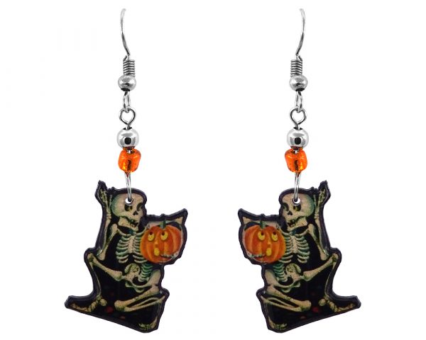 Handmade Halloween themed skeleton holding pumpkin graphic acrylic dangle earrings with beaded metal hooks in beige, black, orange, and yellow color combination.